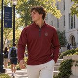 College-aged man wearing a maroon Cutter + Buck Adapt quarter zip with embroidered chest crest and khaki pants while walking outdoors on a college campus.