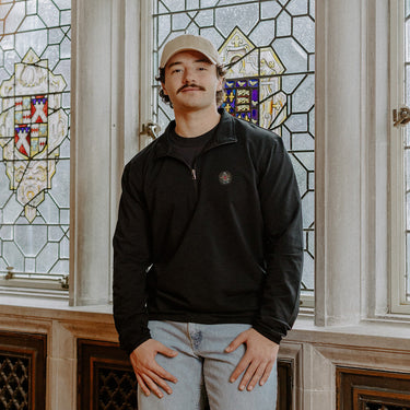 Male model wearing the black Pi Kappa Alpha Embroidered Luxe Quarter Zip in front of stained glass windows with fraternity crests.