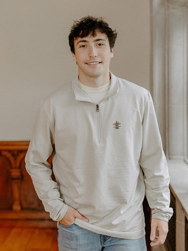 Male model wearing the smoke-colored Pi Kappa Alpha Embroidered Luxe Quarter Zip with crest embroidery, standing by a window in a formal setting.