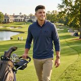 Fraternity man wearing a navy quarter zip pullover walking on a golf course with golf bag, showcasing printed Greek letters apparel