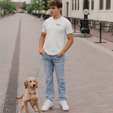 Pike Greek letters on a white short sleeve t-shirt featured on a fraternity member walking a dog.