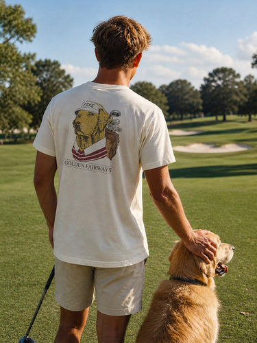 Lifestyle photo of a college student wearing a golf-themed fraternity t-shirt on a golf course with a golden retriever. Ivory Comfort Colors tee features a “Golden Fairways” back graphic with a golden retriever in golf apparel and golf clubs, perfect for fraternity golf tournaments, campus events, and casual Greek life apparel.