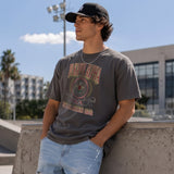 College-aged male wearing the fraternity Collegiate Crest Graphic Tee in charcoal grey, featuring vintage Pi Kappa Alpha crest artwork on campus.